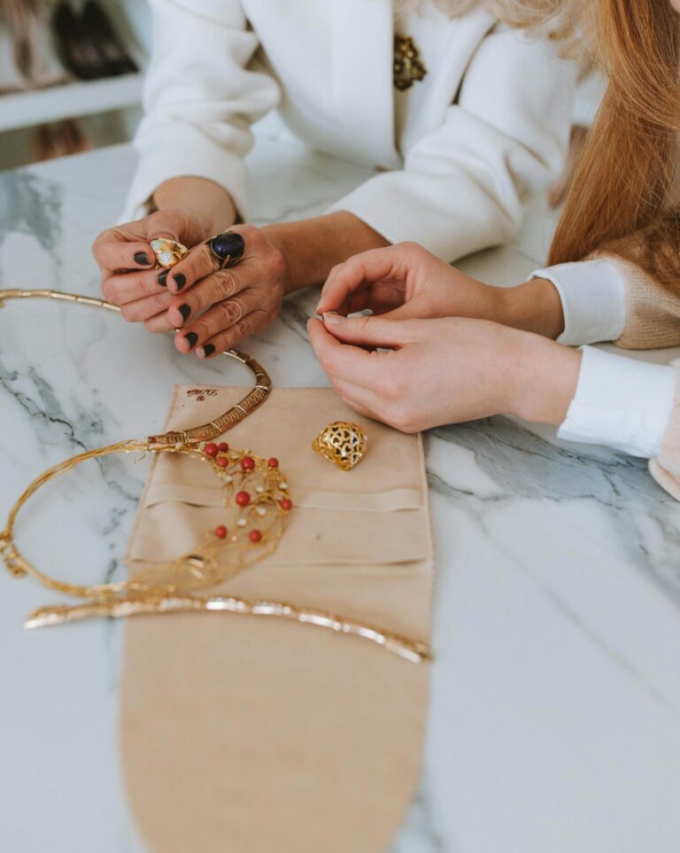 Close-up of hands examining elegant jewelry on a marble table, showcasing craft and detail.